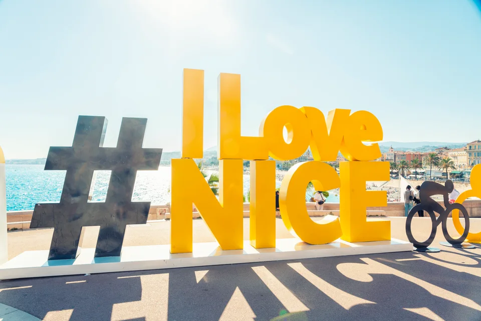 Жёлтая надпись «I Love Nice» на фоне моря и набережной