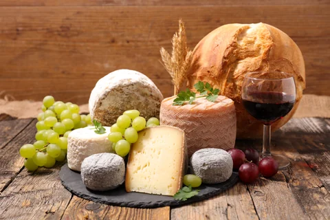 Quesos franceses, pan, uvas y una copa de vino tinto