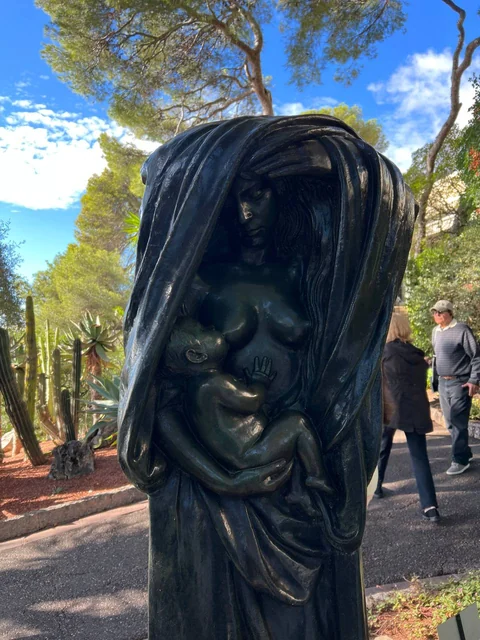 Una escultura de bronce de una mujer con un niño entre los árboles